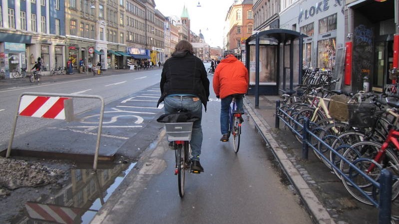 Provisional solution for bus stop platform on Nørrebrogade (2010). There is dedicated space for embarking and disembarking the bus, but passengers still have to cross the bicycle path to reach it from the shelter.